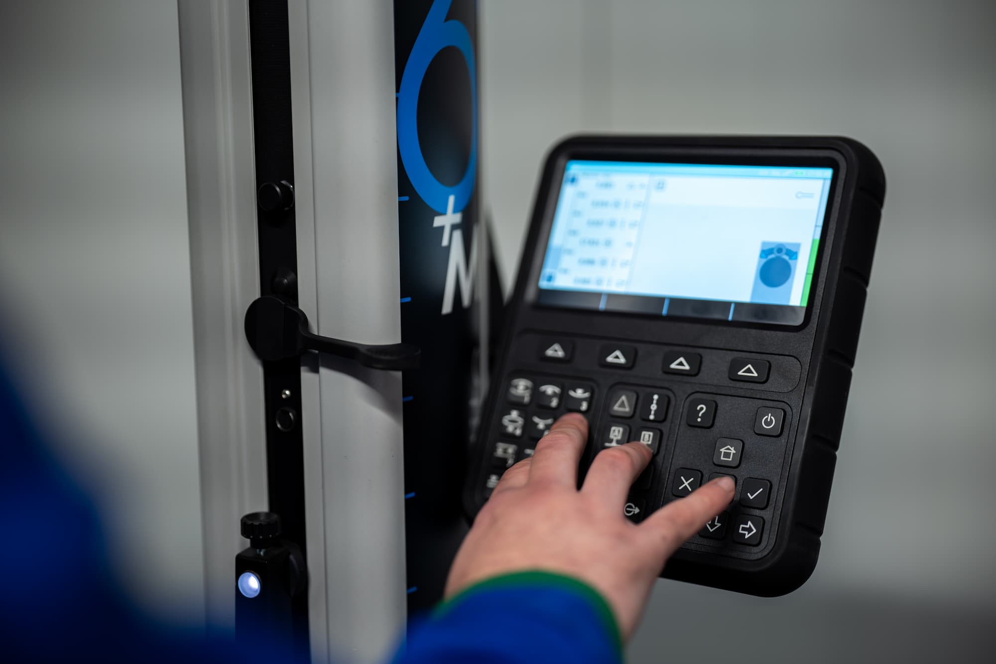 Main d’un technicien utilisant le pupitre de commande d’une machine de mesure tridimensionnelle pour le contrôle qualité.