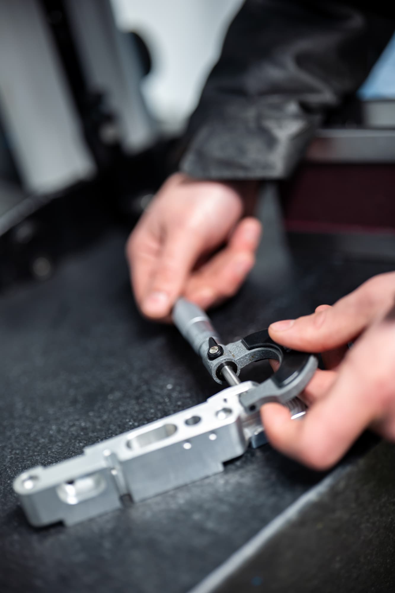 Technicien en atelier d’usinage industriel mesurant une pièce mécanique en aluminium avec un micromètre de précision pour assurer le respect des tolérances dimensionnelles.